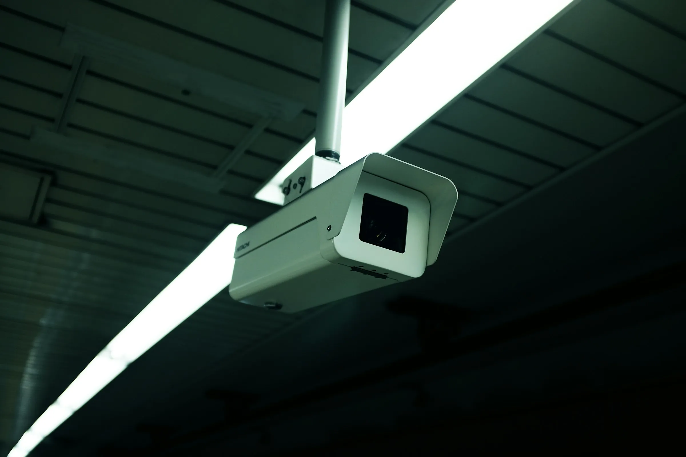 Caméra de surveillance fixée sous un néon, dans un bâtiment industriel sombre.