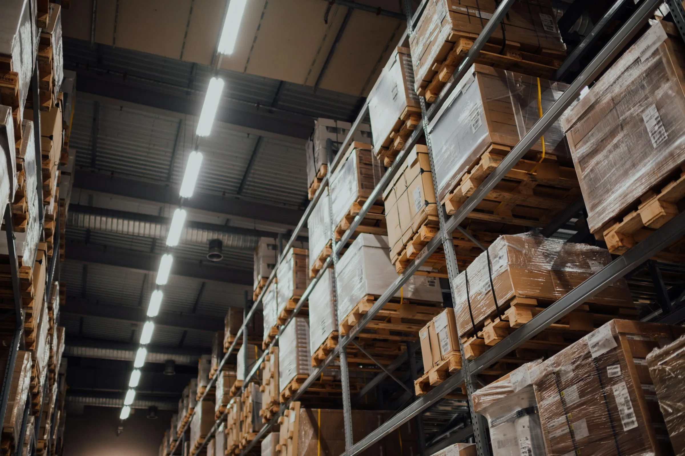 Allée d'un entrepôt logistique, rayonnages chargés de palettes sous un éclairage industriel.