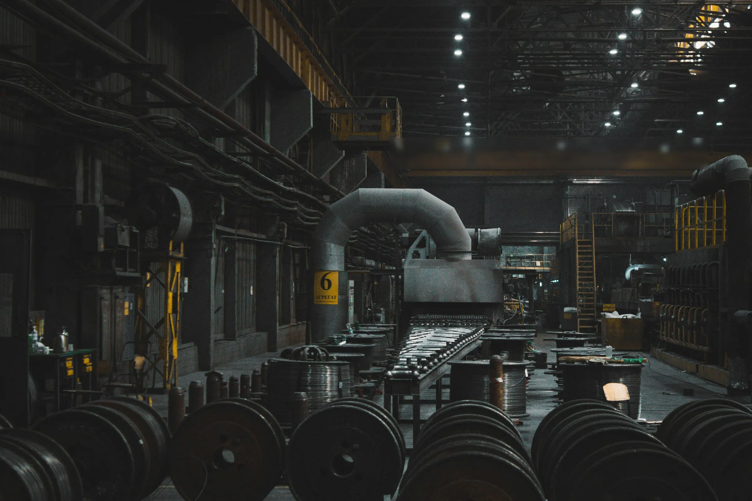 Halle d’usine sombre, bobines métalliques au premier plan.